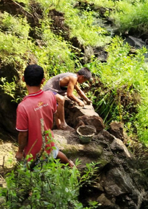 Warga bekerja bersama memperbaiki saluran air dan struktur batu di area perdesaan.